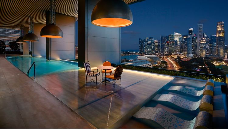 Rooftop pool terrace at the JW Marriott Singapore South Beach, lit at dusk above the city skyline